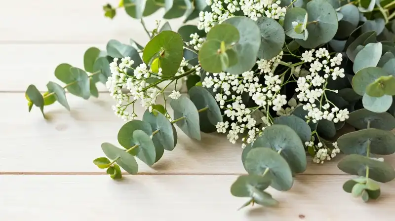 Lush eucalyptus and delicate white flowers rest on soft wooden surface